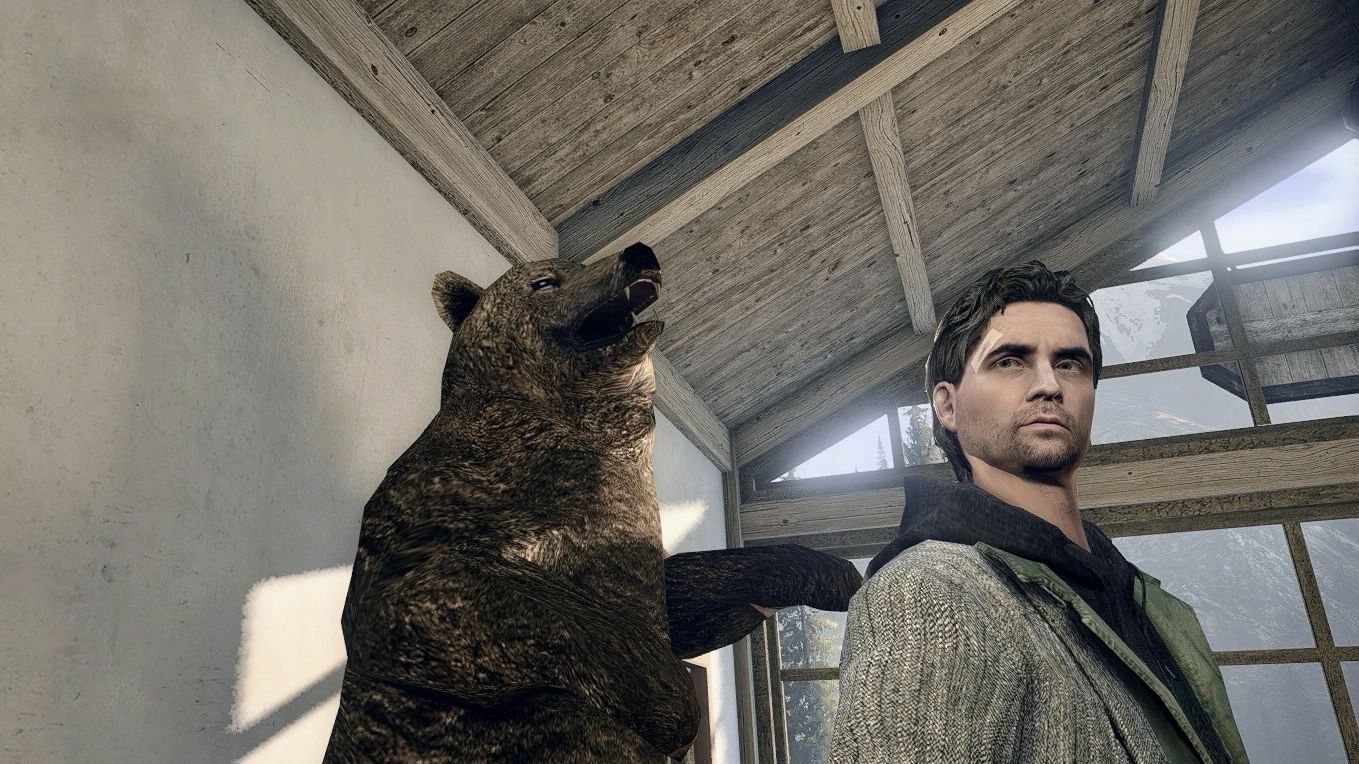 A man with short dark hair and a serious expression stands next to a large, snarling bear taxidermy in a rustic, wooden room with sunlight streaming through the windows.